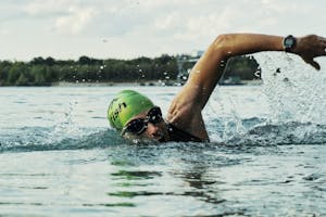 A male swimmer in a green cap and goggles competing in an open water race.