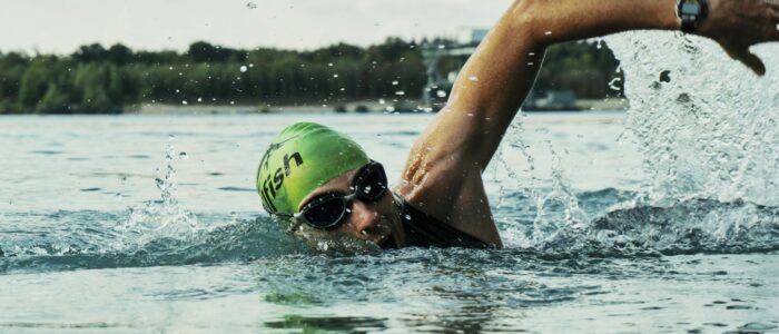 Photo by mali maeder A male swimmer in a green cap and goggles competing in an open water race.