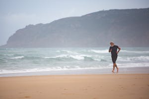 Elderly man maintaining fitness by running along a scenic beach in Portugal.